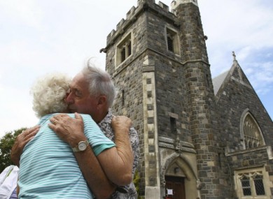 A mourning couple embrace each other in front of damaged church after observing two minutes of silence to mark the time of the earthquake.