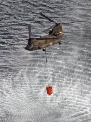 A helicopter scoops water off Japan's northeast coast on its way to the Fukushima Dai-ichi nuclear power plant in Okumamachi Thursday morning.