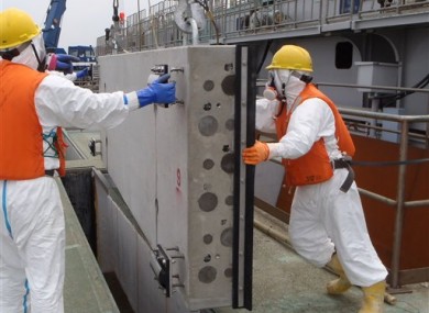 Masked workers in protective outfits prepare to drop one of sliding concrete slabs into a slit of the upper part of the sluice screen for Unit 2 reactor, Fukushima.