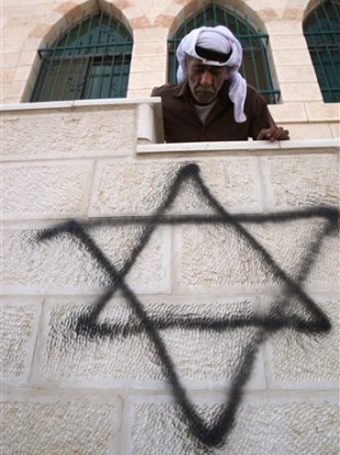 A Palestinian man looks down on a graffiti of the Star of David spray painted on a wall of a mosque torched and vandalized by arsonists in the West Bank village of Qusra, near Nablus, Monday, Sept. 5, 2011.