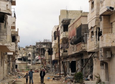Syrians walk between destroyed buildings in the Inshaat neighborhood of Homs, Syria