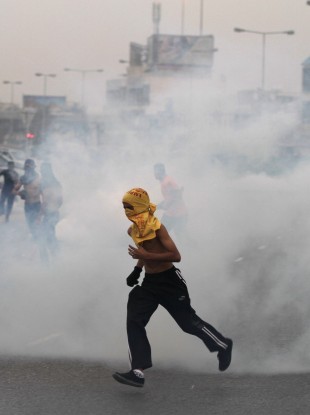 Anti-government protesters run through tear gas fired by riot police Friday, April 20, 2012