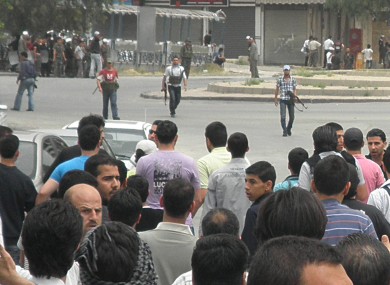 Syrian security forces, background, hold their machine guns and surround anti-Syrian regime mourners, foreground, in Damascus