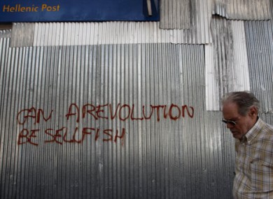 A Greek man walks past metal sheeting sprayed with a slogan in English reading