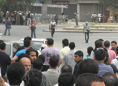 Syrian security forces, background, hold their machine guns and surround anti-Syrian regime mourners, foreground, during the funeral procession in April