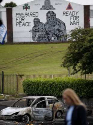 A woman walks past a burnt out car in the Mount Vernon area of north Belfast on Tuesday.