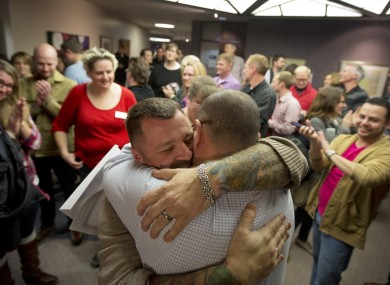 Chris Serrano, left, and Clifton Webb embrace after being married, as people wait in line to get licenses in Salt Lake City.