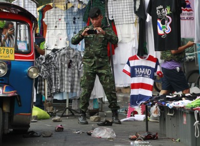A soldier photographs the scene of an explosion littered with blood and small pairs of shoes at a main protest site in Bangkok.