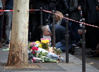 A man holds his head in his hands beside flowers paying tribute to the victims of Friday night's attacks.