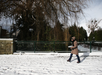 A woman walking through Glasnevin in Dublin during the snow.