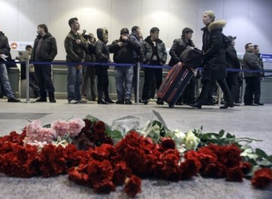 A woman pushes her luggage past flowers at the site of Monday's explosion at Domodedovo.
