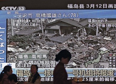 A hostess at China's National People's Congress, in Beijing, passes a TV screen showing the damage to the Japanese prefecture of Fukushima, home to the stricken Fukushima I nuclear plant.