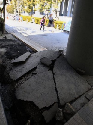 People walk past a damaged road outside of Tokyo Disneyland in Urayasu, east of Tokyo, Japan, Tuesday, March 29, 2011. Tokyo Disneyland was shut down after the March 11 earthquake and has been closed ever since.