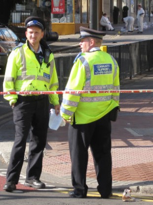 Police on Spring Bridge Road in Ealing where a man suffered life-threatening injuries when he was attacked by rioters after he tried to extinguish a fire they had started in a bin.