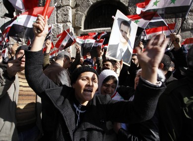 Mourners wave Syrian flags and a photo of President Bashar Assad as they chant slogans at a mass funeral Saturday, Dec. 24, 2011
