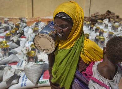 File: A woman carries a child and a tin of vegetable oil she just received at a food distribution center in Mogadishu, Somalia.