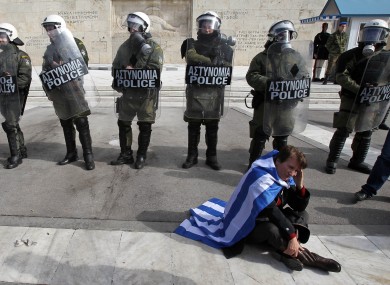 A protester wearing a Greek flag sits in front of riot police during a rally outside the Greek Parliament yesterday.