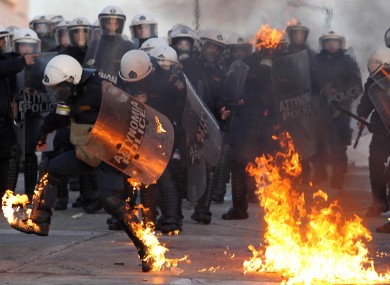 A riot police officer tries to extinguish flames from a petrol bomb thrown by protestors outside the Greek parliament.