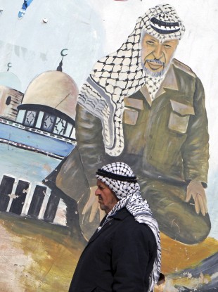 An elderly Palestinian walks next to a mural depicting Yasser Arafat, in the northern West Bank village of Kabatyeh.