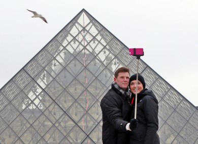Chris Baker and Jennifer Hinson from Nashville, Tennessee, use a selfie stick in front of the Louvre Pyramide in Paris.