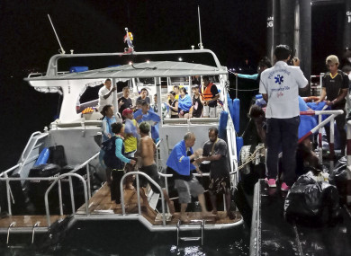 Rescued tourists from a boat that sank are helped onto a pier.