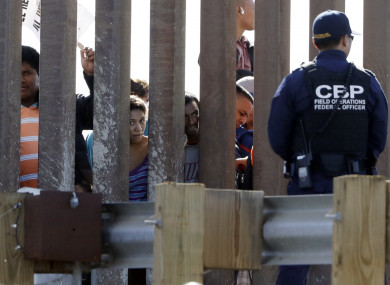 Migrants from Central America look through a border wall into the US