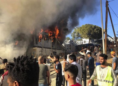 Migrants and refugees stand next to burning house containers at the Moria refugee camp, on the northeastern Aegean island of Lesbos, Greece