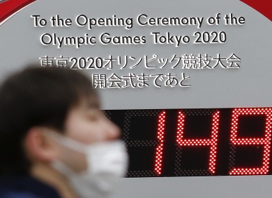 A man wearing surgical mask walks past a countdown clock outside Tokyo Station for the opening ceremony of the Tokyo 2020 Olympic and Paralympic Games.