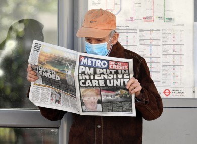A man wearing a facemask at a bus stop reading a newspaper outside St Thomas' Hospital in Central London.