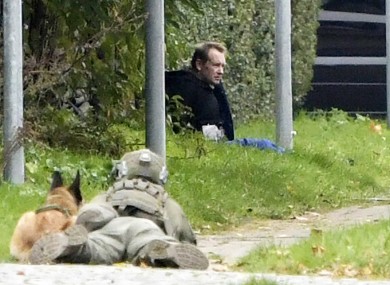 A police office watches Peter Madsen as he sits on the side of a road after being apprehended.